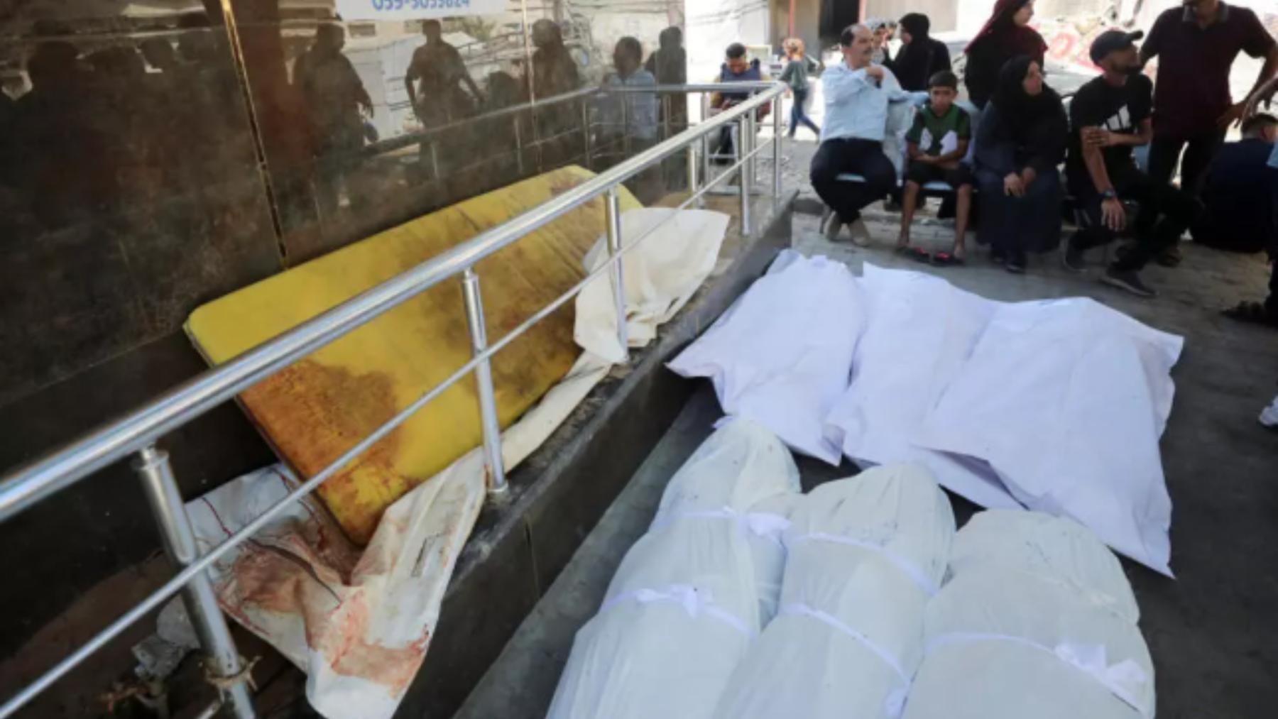 Los dolientes se sientan junto a los cadáveres durante el funeral de los palestinos muertos en un ataque israelí nocturno contra una casa