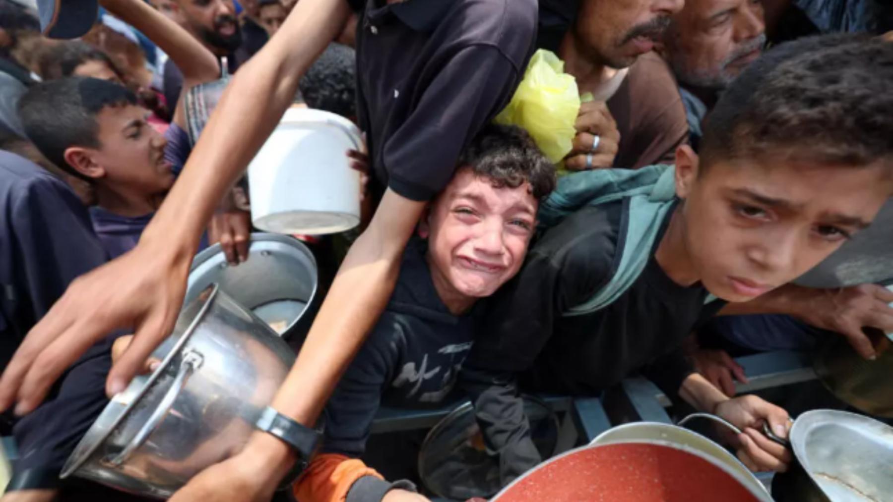 Niños reaccionan mientras la gente hace fila para recibir alimentos en un punto de distribución en Nuseirat