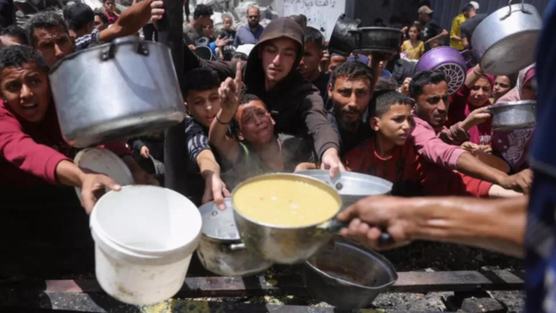 Palestinos desplazados se reúnen para recolectar porciones de comida cocinada en una distribución benéfica en Jabalia, al norte de la Franja de Gaza, el 19 de mayo de 2025.